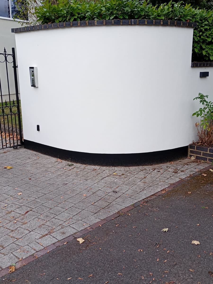 Curved rendered garden wall painted white with a black plinth, beside a block-paved driveway