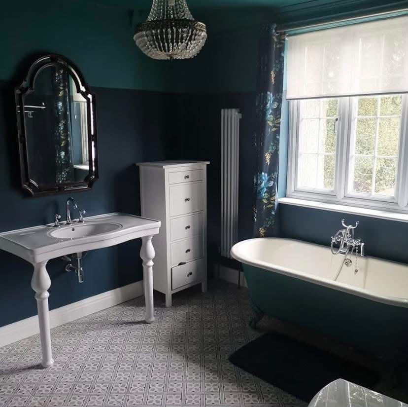 Bathroom painted in dark green and navy with a white roll-top bath and white woodwork