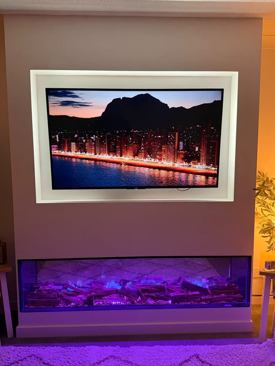 Media wall painted white with a TV set in a recessed frame above a long electric fire