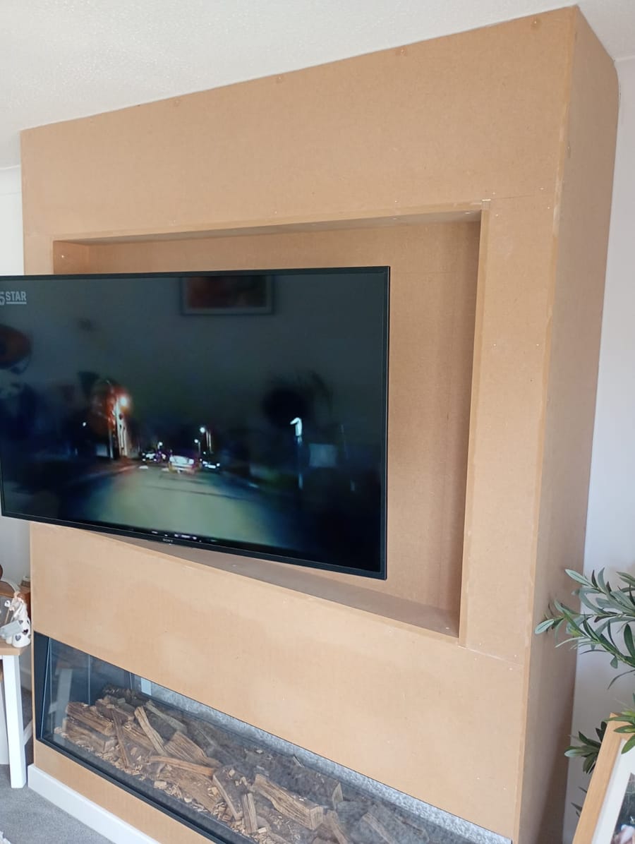 Media wall frame in bare MDF with the TV fitted and a log-effect fire below