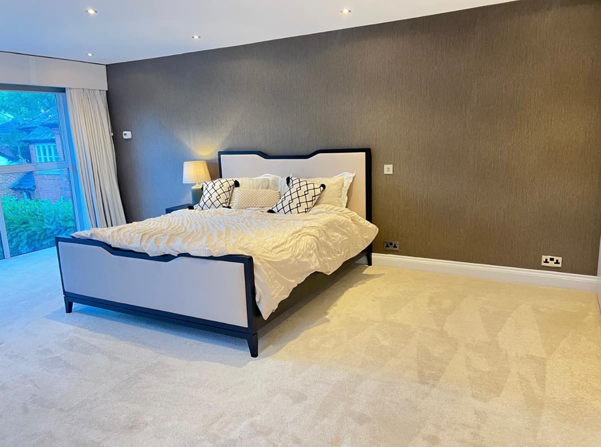 Bedroom with a textured brown wallpaper wall between a full-height window and fitted wardrobes